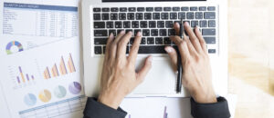 Top view of businesswoman’s hands working with laptop on wooden table.